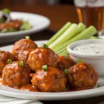 Buffalo chicken meatballs coated in spicy sauce, served with ranch dip and celery on a rustic wooden table.